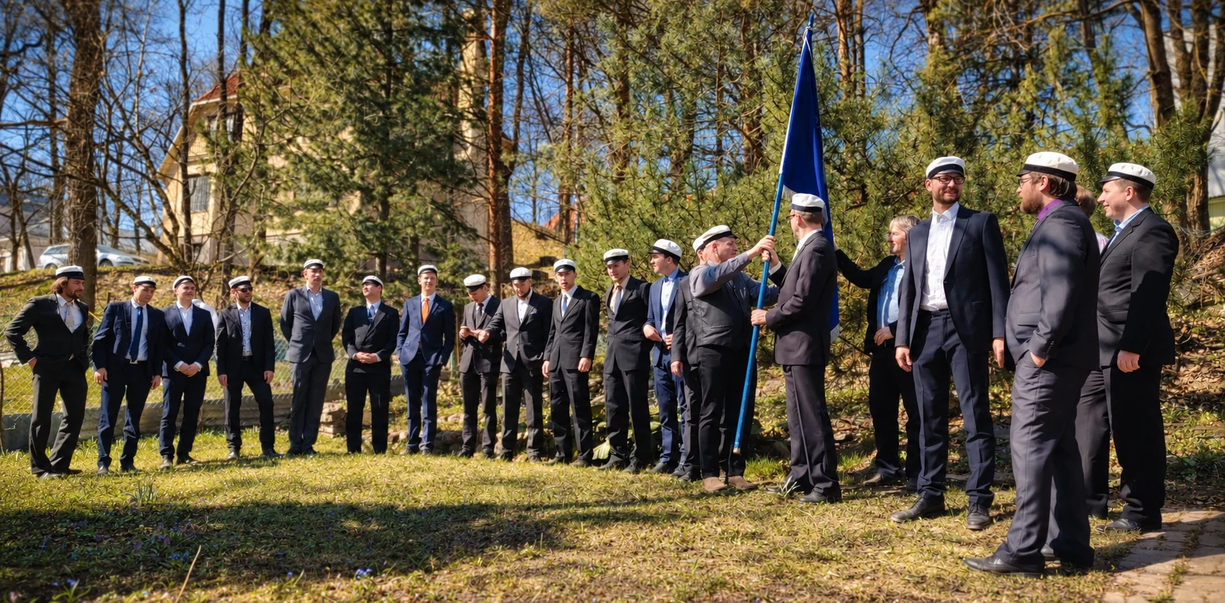 Liiviklased valgetes üliõpilasmütsides seltsi lipuga seltsi aias aastapäeval