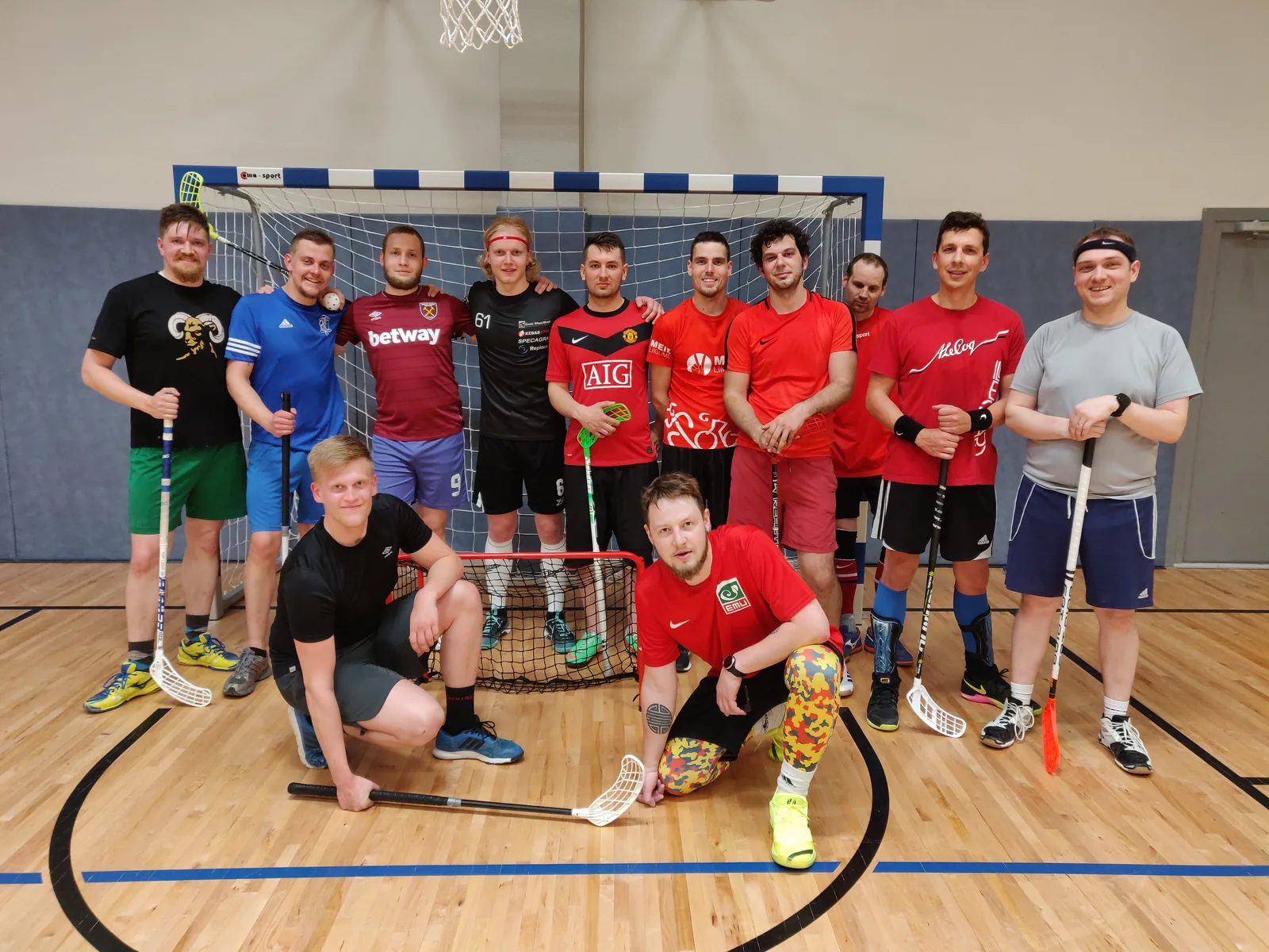 Kaksteist saalihokimängijat kepidega spordisaalis värava ees, mustvalge foto